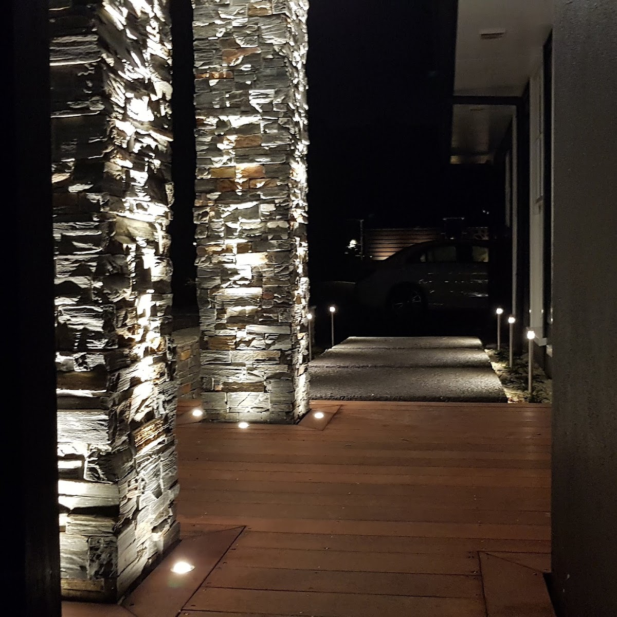 Night exterior lit by Rob Tiatia Electrical, stone columns uplit with warm path and deck lighting